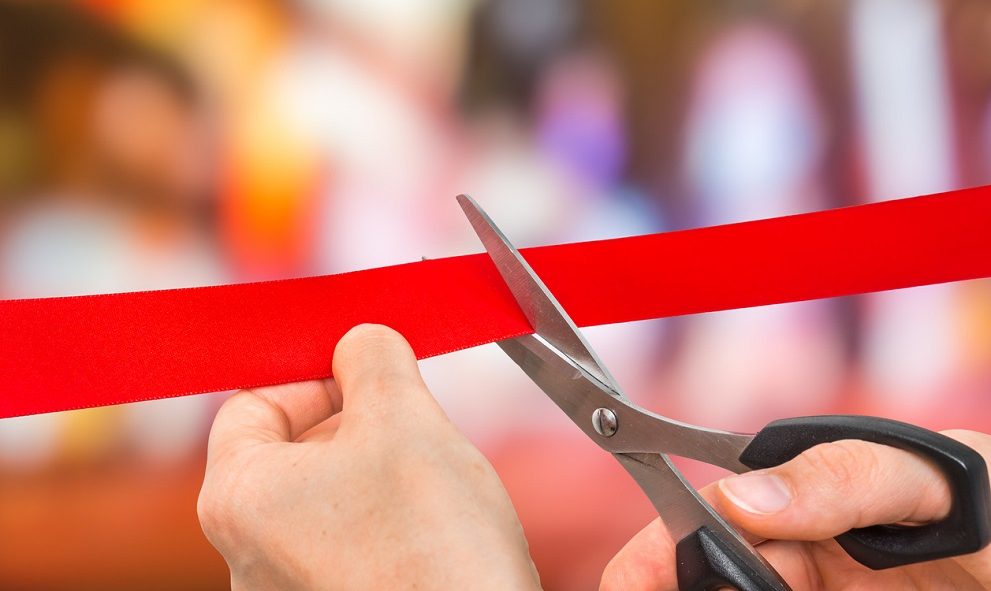 Hand with scissors cutting red ribbon